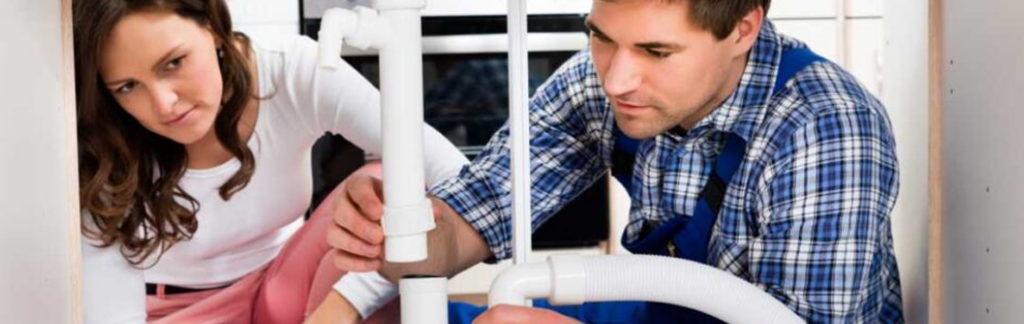 A plumber fixing a leaky faucet under a kitchen sink with various plumbing tools nearby.