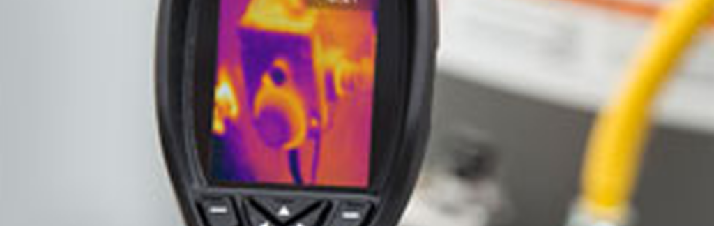 A plumber using a thermal imaging camera to identify a water leak behind a bathroom wall.